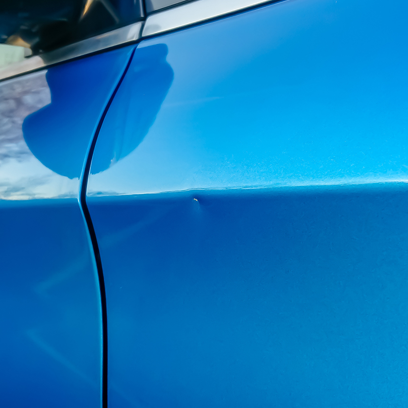 Bosse dans la portière d’une voiture bleue